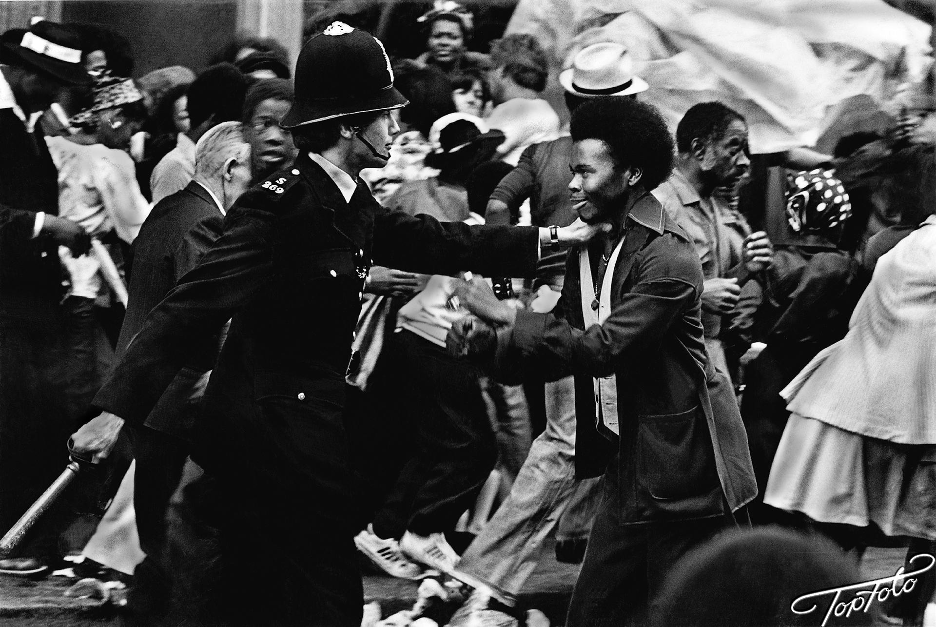 At the 1976 Notting Hill Carnival the police surrounded the festivities and, to everyone's surprise, they attacked the crowd. Here is one moment when a strange confrontation took place as they are surrounded by the chaos. August 1976